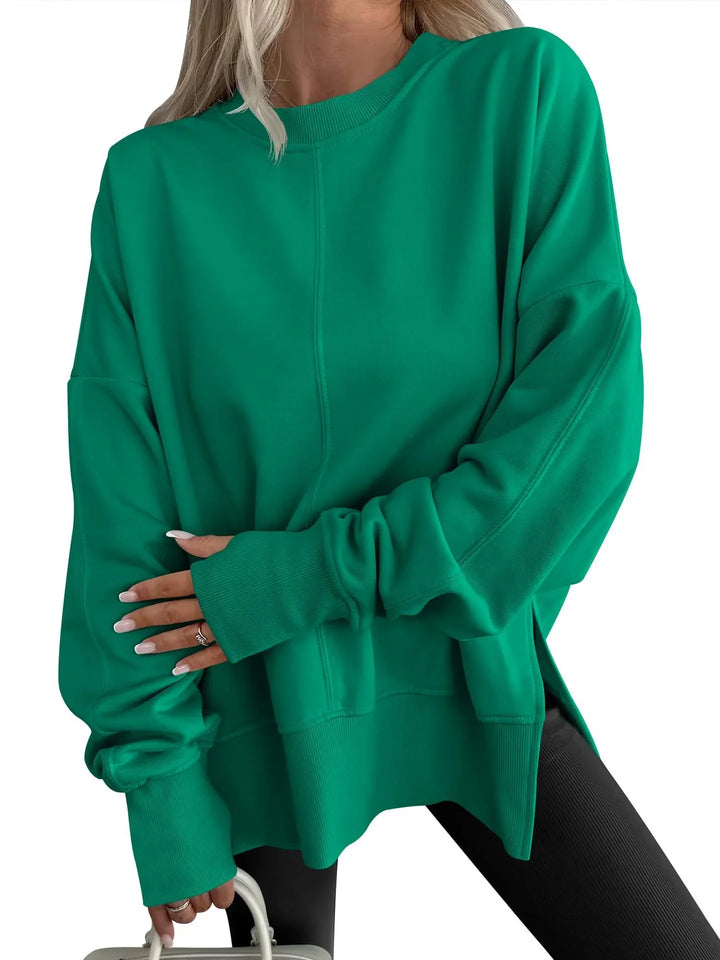 Woman wearing oversized green sweatshirt with ribbed cuffs and black leggings holding white bag