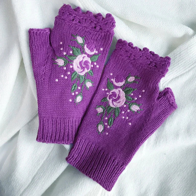 Purple knitted fingerless gloves with embroidered floral design resting on white fabric