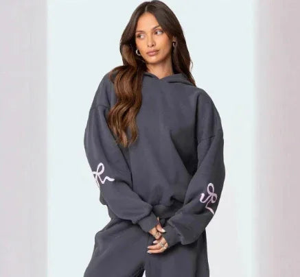 woman wearing charcoal gray hoodie and matching sweatpants with script detail on sleeves