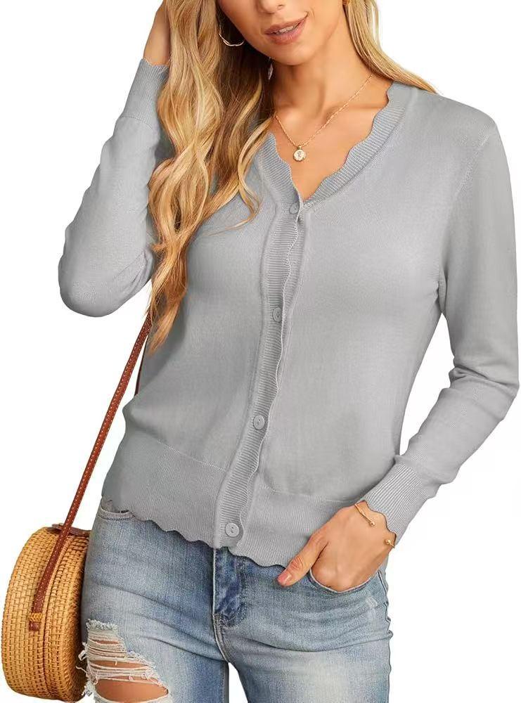 Woman wearing light gray buttoned cardigan with scalloped edges, distressed jeans, and round wicker handbag