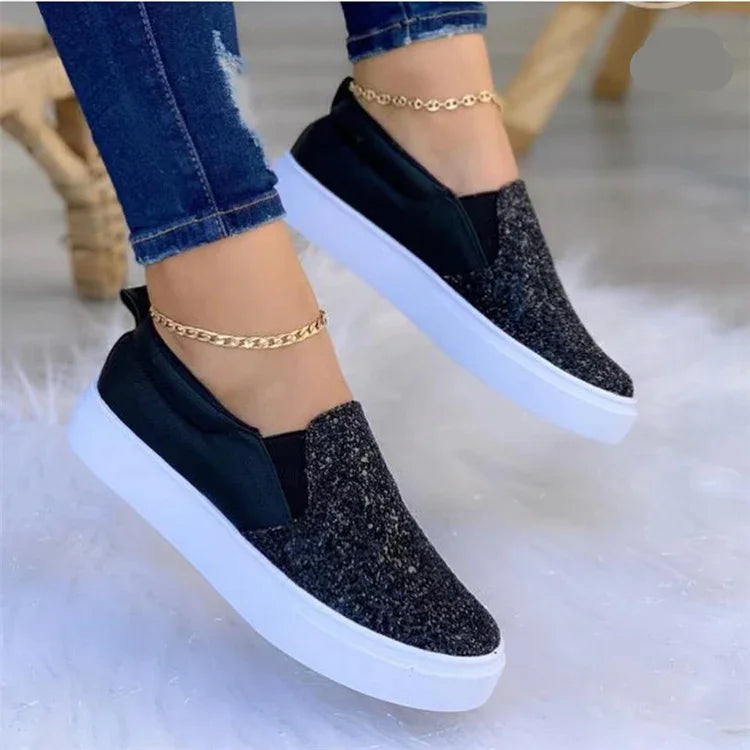 Black slip-on sneakers with glitter texture and white soles worn with blue jeans and gold anklets