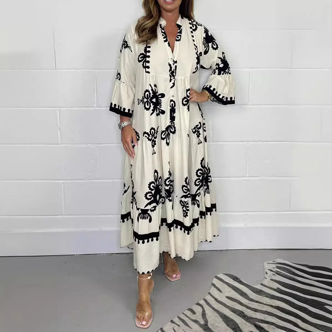 Woman wearing a long beige dress with black floral embroidery standing indoors on gray floor next to zebra rug