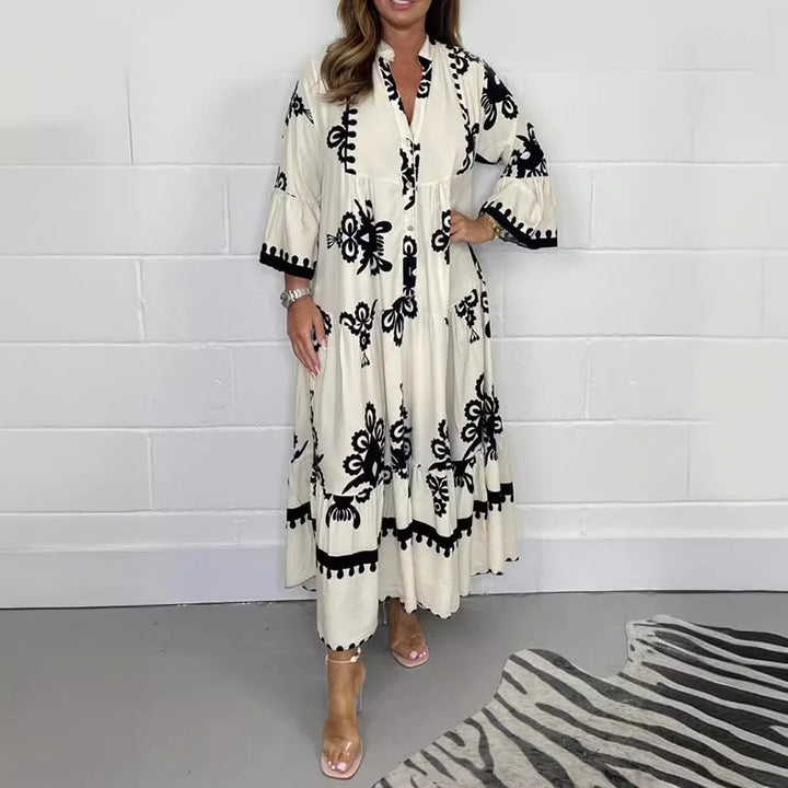 Woman wearing a long beige dress with black floral embroidery standing indoors on gray floor next to zebra rug