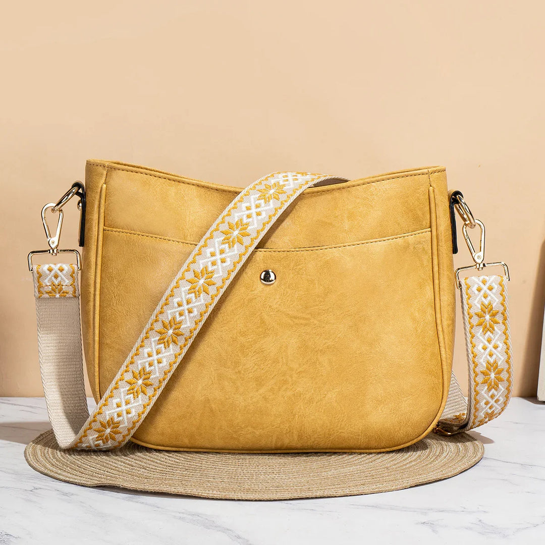 Mustard yellow leather crossbody bag with white and yellow embroidered adjustable strap on round mat