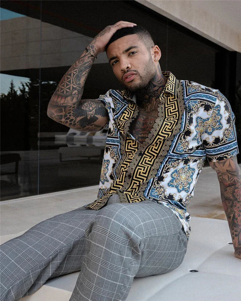 Tattooed man with nose ring wearing patterned short-sleeve shirt and gray plaid pants sitting outdoors