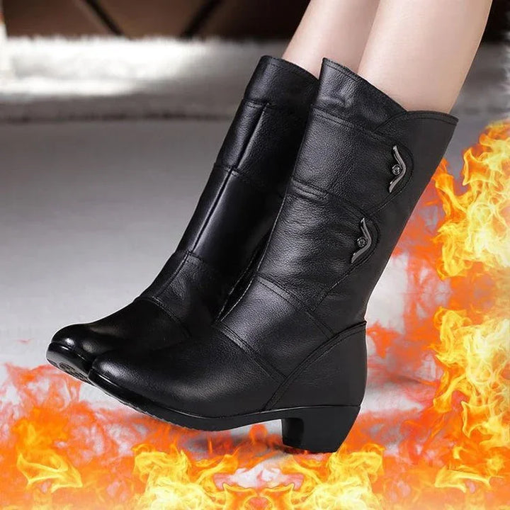 Black mid-calf leather boots with low heels and decorative buttons on white floor surrounded by flames