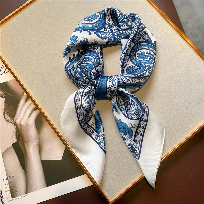 Blue and white paisley patterned silk scarf neatly folded on a beige surface with a framed black and white photo partially visible