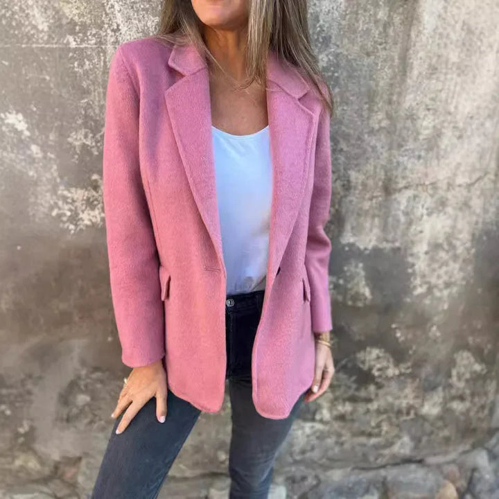 Woman wearing pink wool coat with white top and dark jeans against textured wall