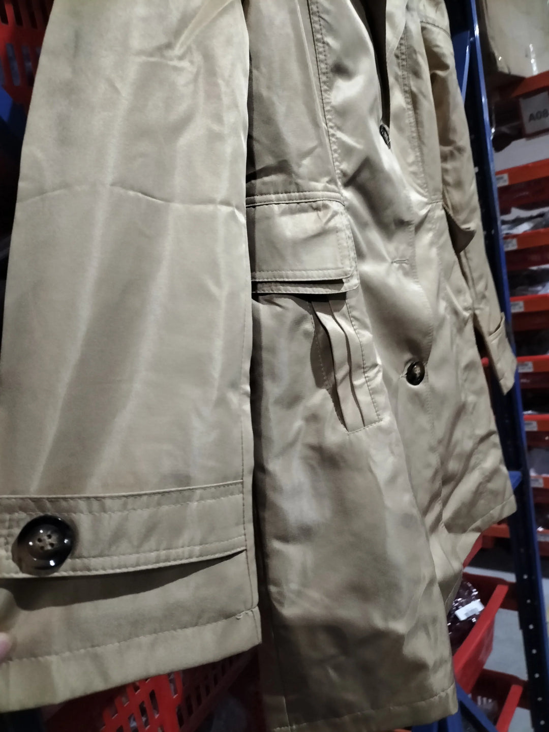 Close-up of beige trench coat with buttoned cuff and flap pocket in retail clothing warehouse