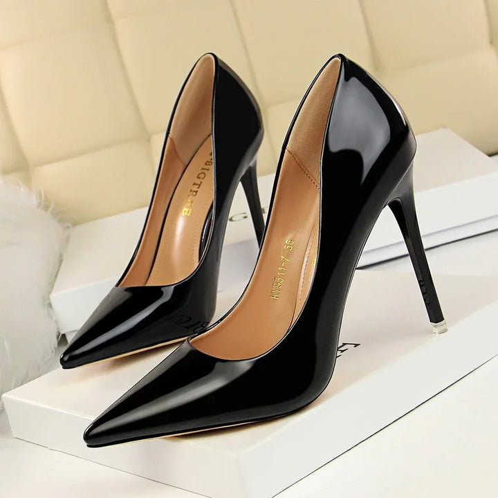 Glossy black high-heeled pointed toe pumps on white boxes with beige cushioned background