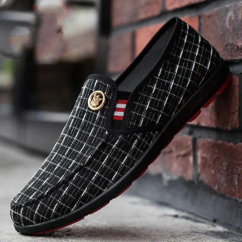 Black and white checkered slip-on shoe with red-striped elastic and gold emblem on brick background