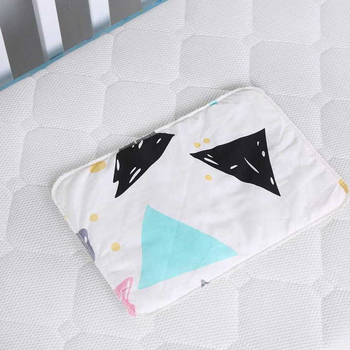 White baby pillow with black, blue, and yellow triangle patterns on a white textured crib mattress