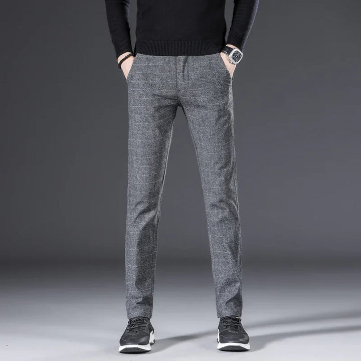 Man wearing slim fit gray plaid dress pants with black sneakers and black sweater on gray background