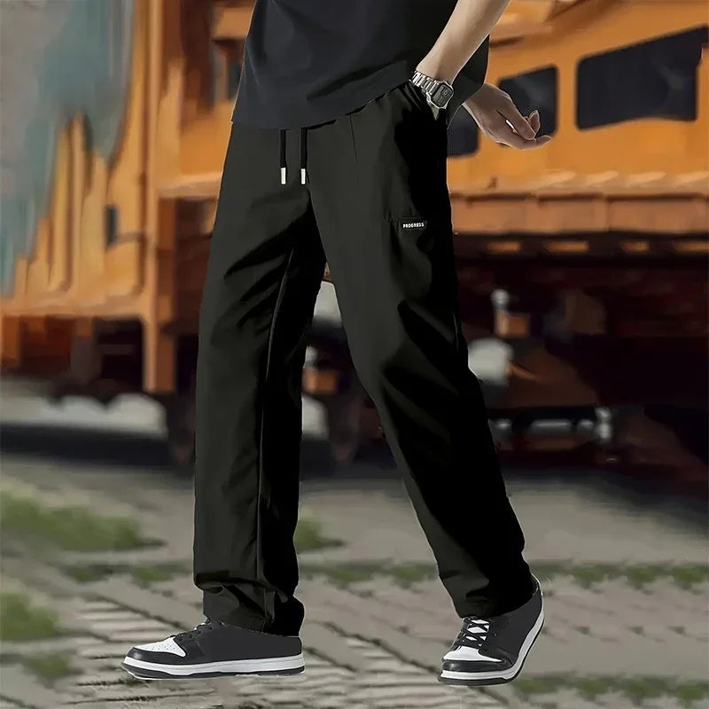 Man wearing black cargo pants with 'PROGRESS' label and black sneakers outdoors