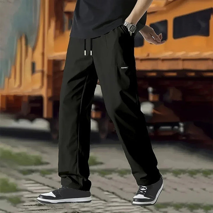 Man wearing black cargo pants with 'PROGRESS' label and black sneakers outdoors