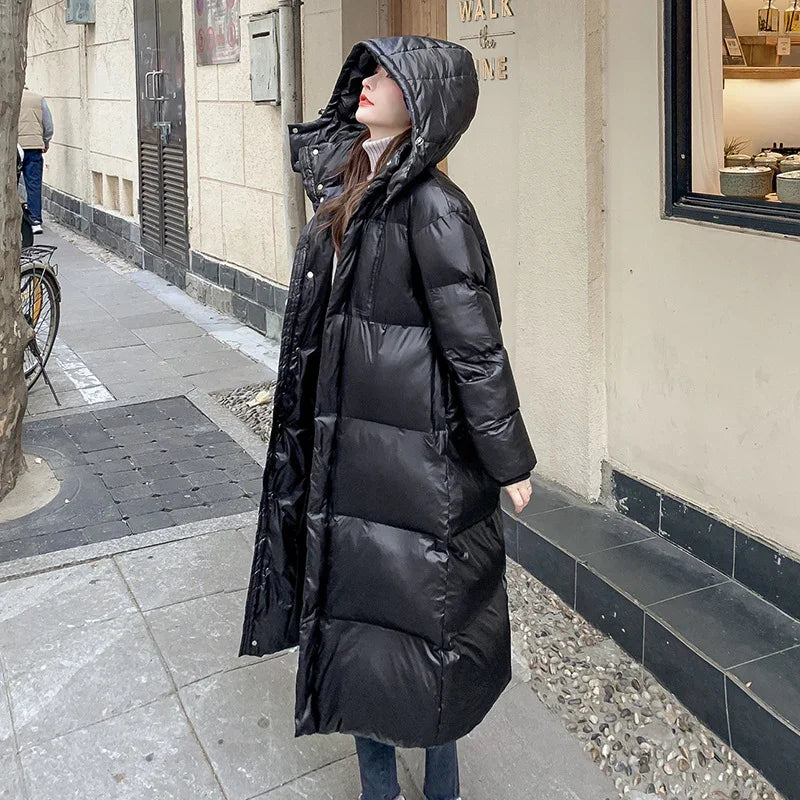 Woman wearing long black puffer coat with hood standing on urban street near building