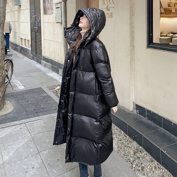 Woman wearing long black puffer coat with hood standing on urban street near building