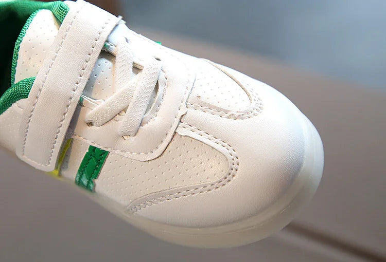 Close-up of white kids sneaker with green accents and Velcro strap on hardwood floor