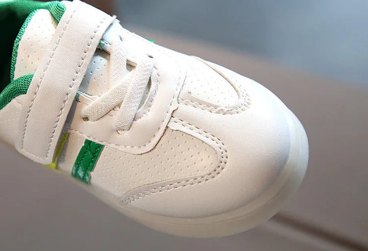 Close-up of white kids sneaker with green accents and Velcro strap on hardwood floor