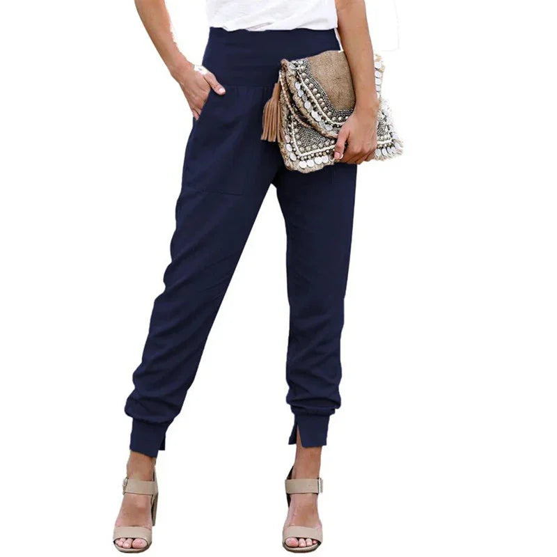 Woman wearing navy jogger pants with cuffed ankles and beige heels, holding a decorative clutch bag