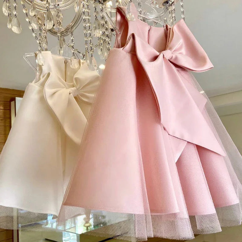 Elegant pink and ivory satin baby dresses with large bows hanging on crystal chandelier