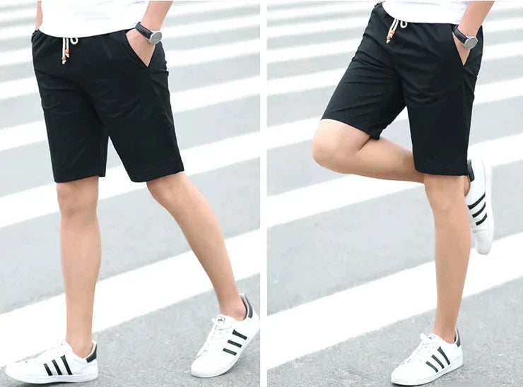 Man wearing black casual shorts and white sneakers with black stripes standing on a pedestrian crossing
