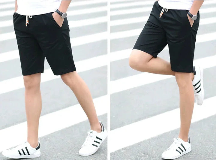 Man wearing black casual shorts and white sneakers with black stripes standing on a pedestrian crossing