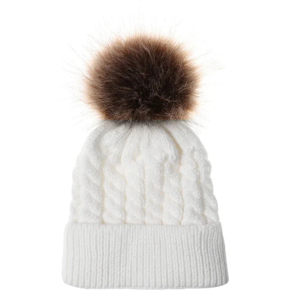White cable knit winter beanie with a large brown faux fur pom pom on top