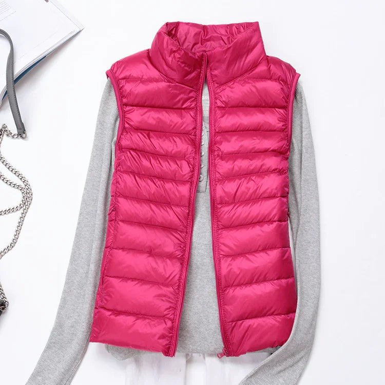 Bright pink sleeveless puffer vest over light gray long sleeve knit sweater on white background