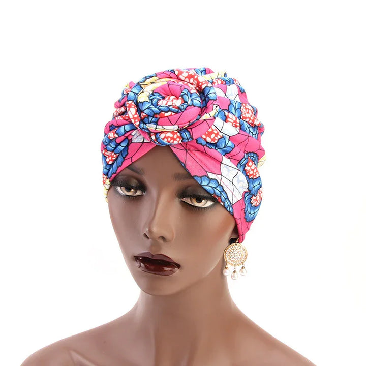Mannequin wearing vibrant pink, blue, white floral turban headwrap with gold and pearl earrings
