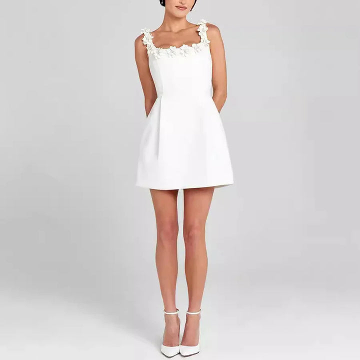 Woman wearing white mini dress with floral straps and white ankle-strap heels on gray background