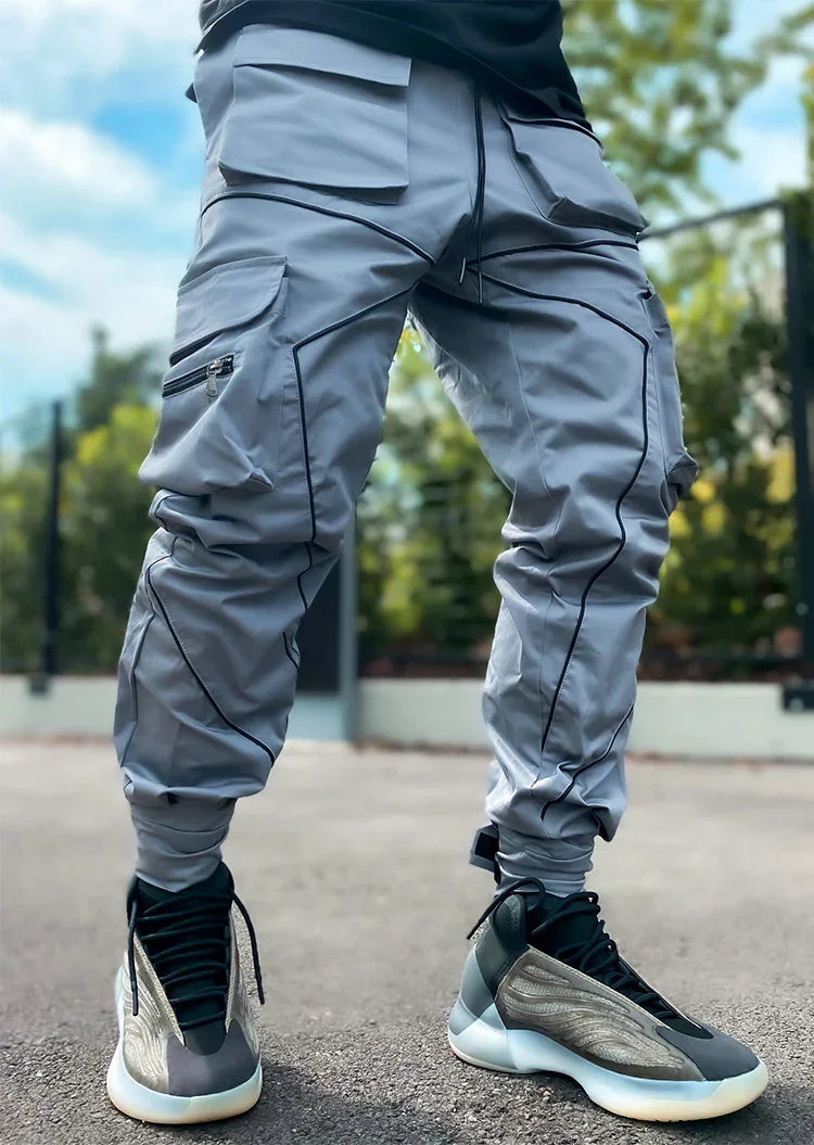 Person wearing light gray cargo pants with black piping and black-gray sneakers standing outdoors