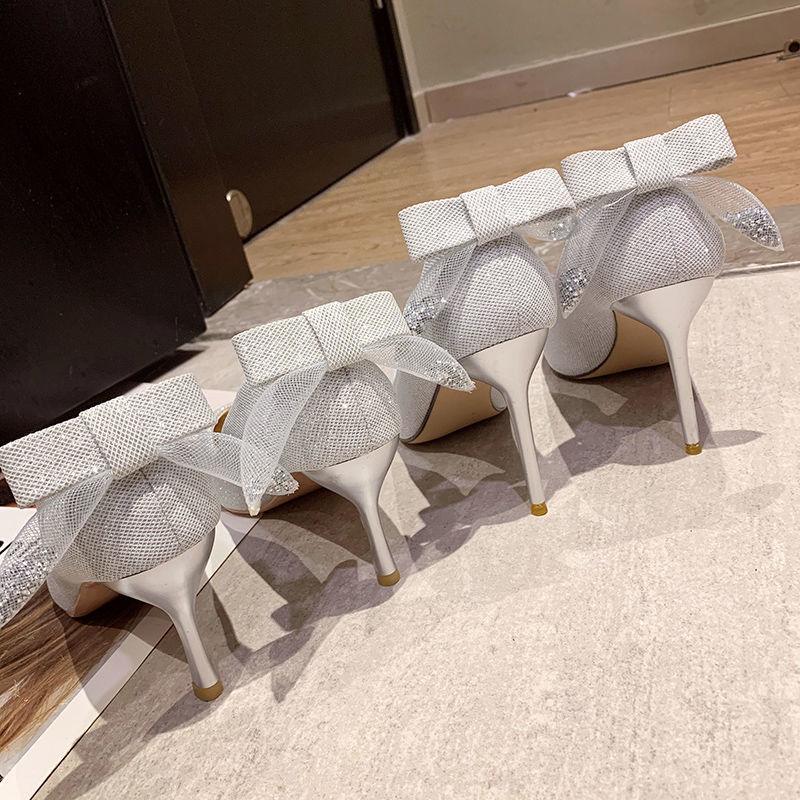 Pair of elegant white high heel shoes with textured fabric and ankle bows on hardwood floor