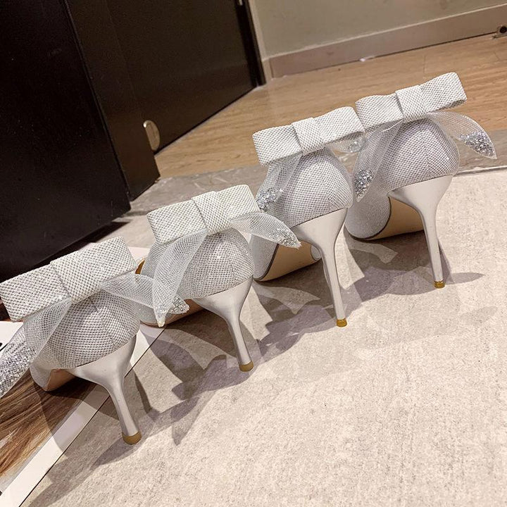 Pair of elegant white high heel shoes with textured fabric and ankle bows on hardwood floor