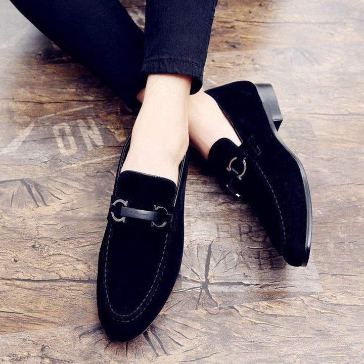 Black suede men's loafers with metal bit detail on wooden floor, paired with black pants