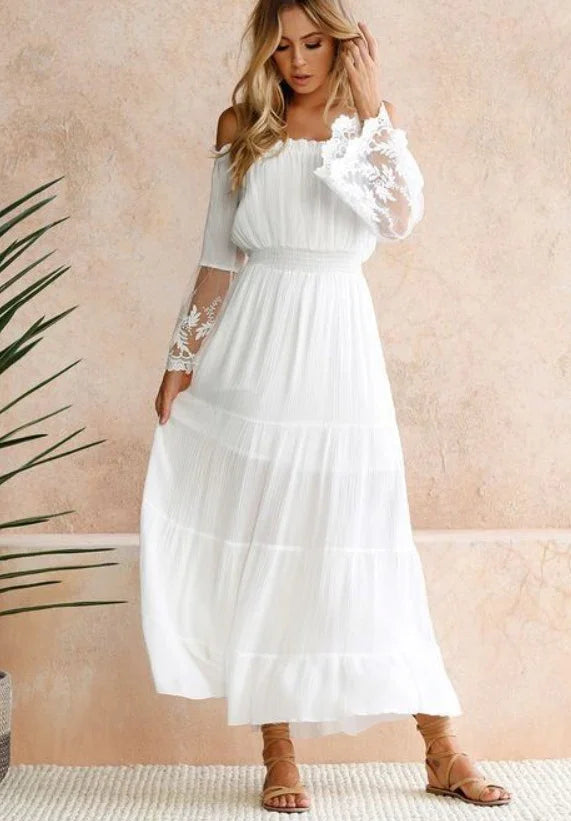 Blonde woman wearing a white off-shoulder lace sleeve maxi dress with strappy sandals, indoor setting