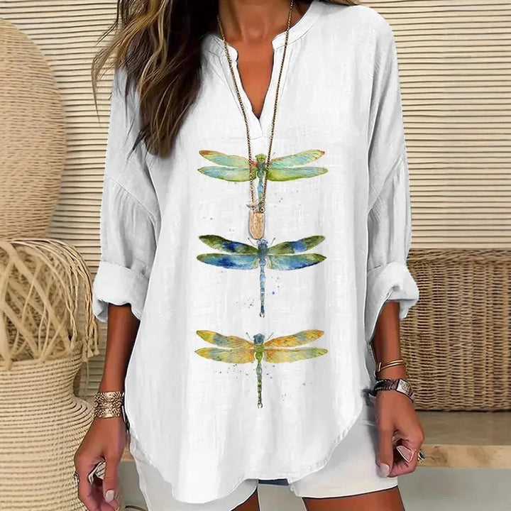 Woman wearing white blouse with colorful dragonfly prints, standing in a wicker and rattan indoor setting