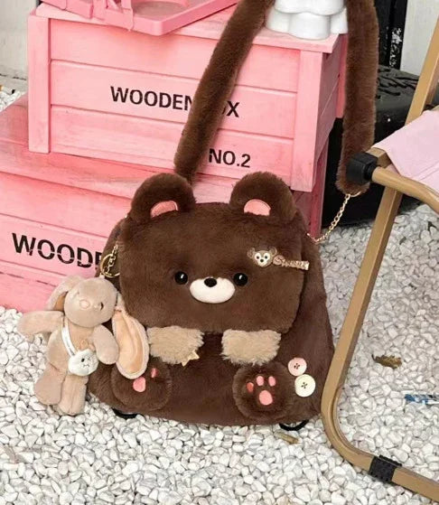 Brown plush bear bag with pink paw details and attached bunny keychain on white pebble floor