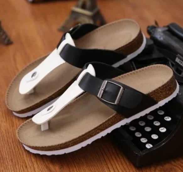 Black and white thong sandals with buckle on cork sole placed on wooden surface near vintage calculator