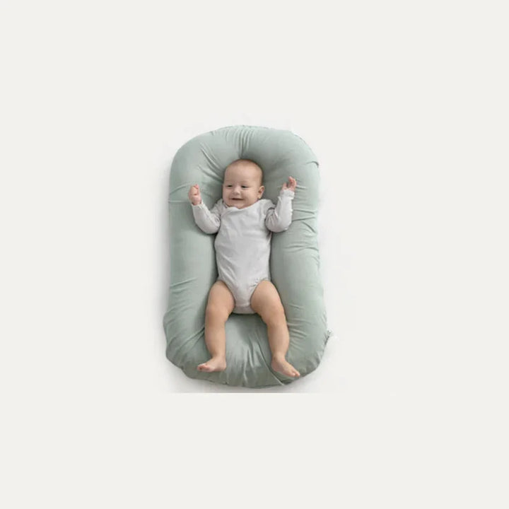 Smiling baby lying on light green baby lounger pillow against white background
