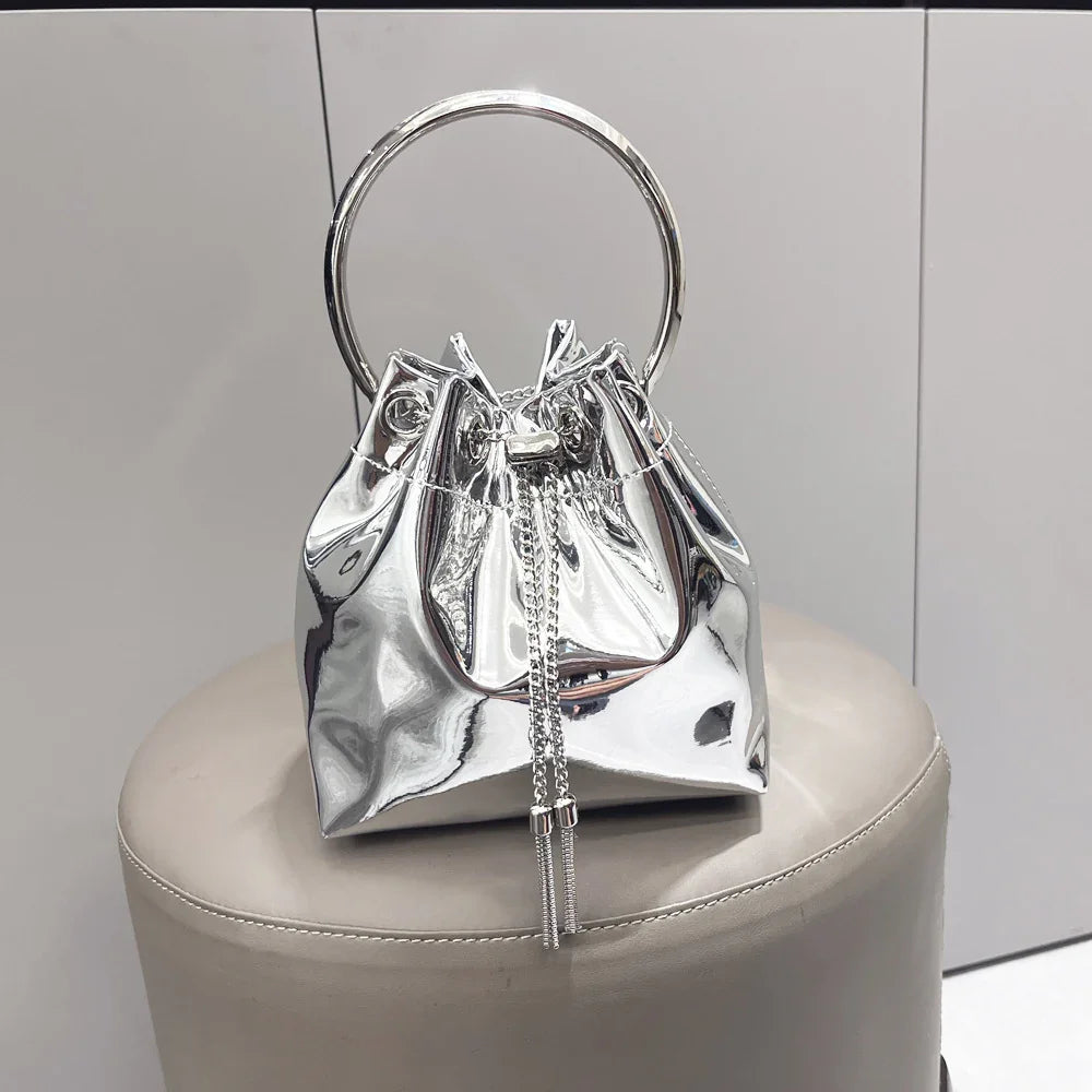 Shiny silver metallic handbag with large circular handle and chain drawstring on beige stool