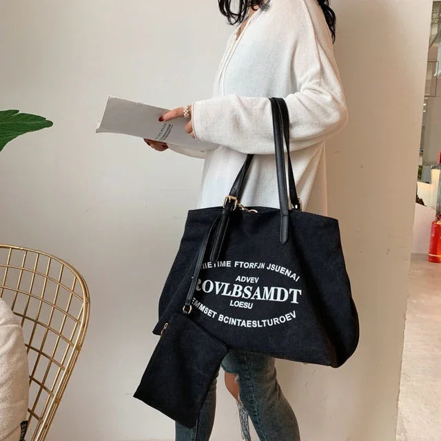 Woman wearing white sweater and jeans holding black tote bag with white random text in indoor setting