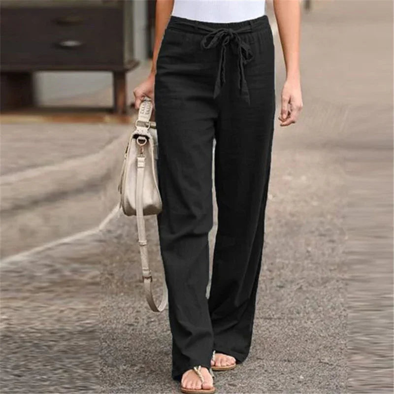 Woman wearing black drawstring wide-leg pants walking outdoors with beige handbag and sandals