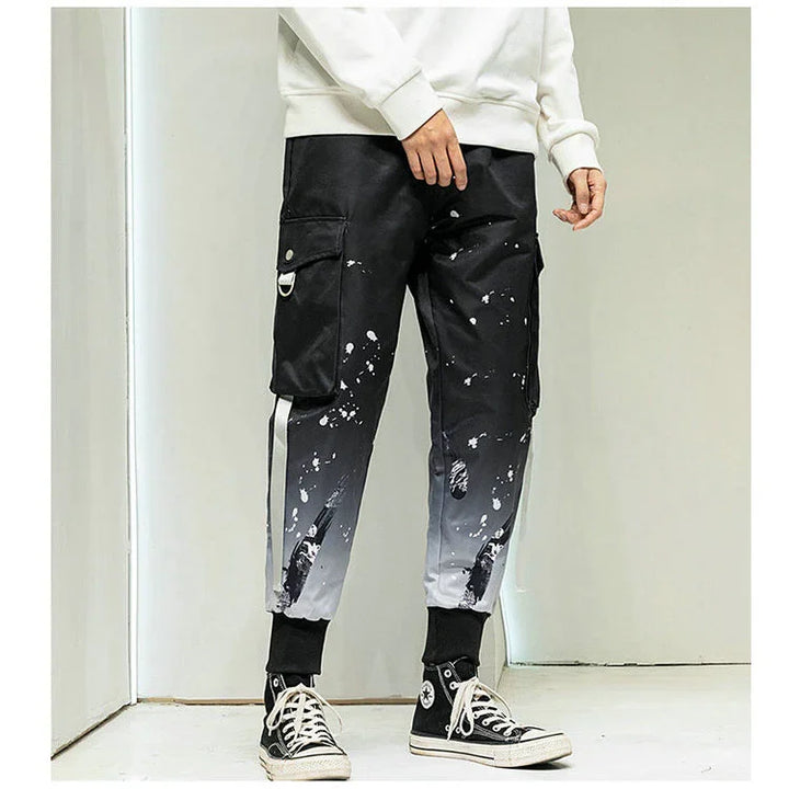 Men's black and gray gradient cargo pants with paint splatter and distressed details, paired with black high-top sneakers