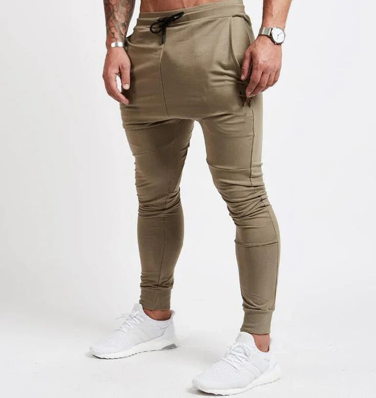 Man wearing beige slim-fit jogger pants with black drawstring and white sneakers on white background