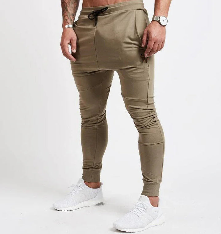 Man wearing beige slim-fit jogger pants with black drawstring and white sneakers on white background