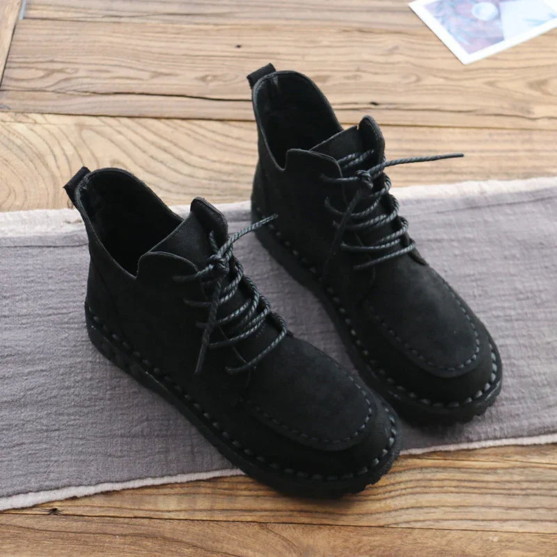 Pair of black suede ankle boots with laces on wooden surface and gray cloth