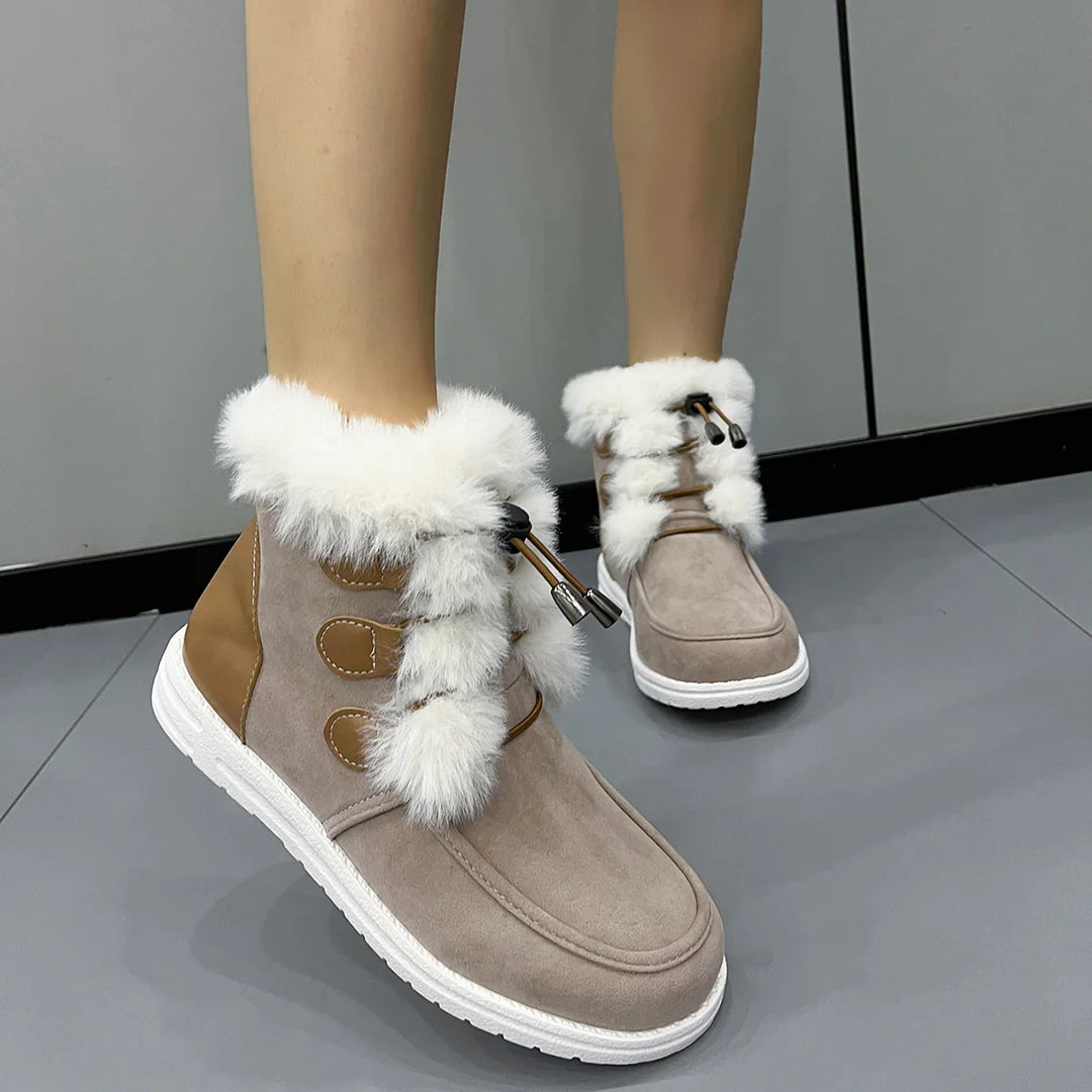 Beige winter boots with white fur trim and white soles worn indoors on gray floor