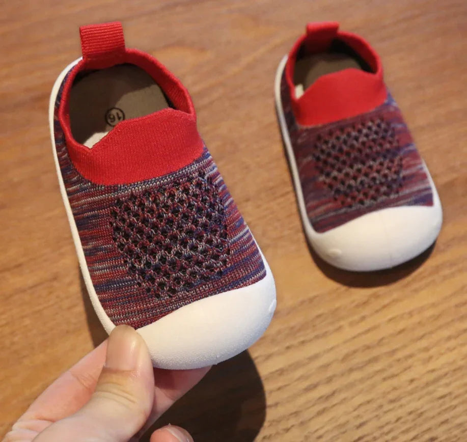 Red and purple toddler slip-on shoes with white rubber toes on wooden surface