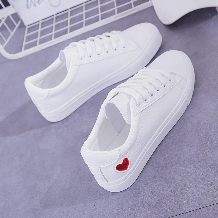 Pair of white canvas sneakers with lace-up design and small red heart detail on side